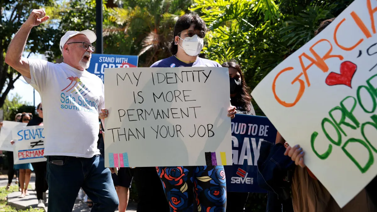 A line of protesters, including one with his hand in the air and one in a mask, carry signs in favor of LGBTQ+ rights.