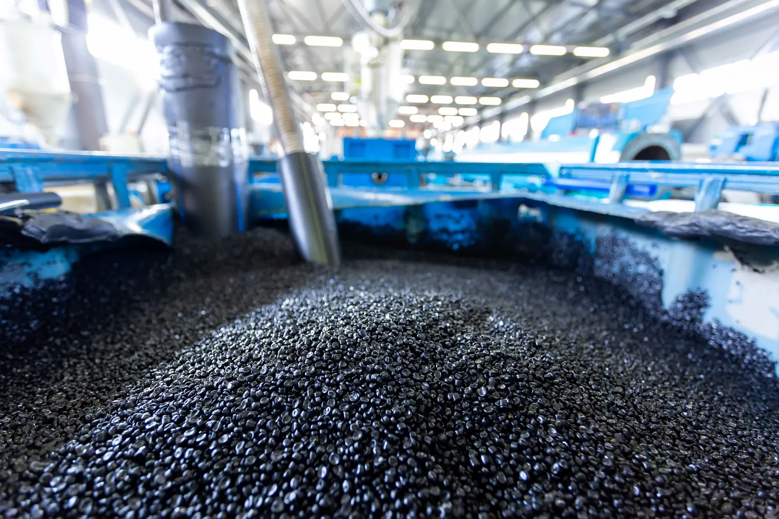 A large tote full of black plastic pellets in a manufacturing facility.