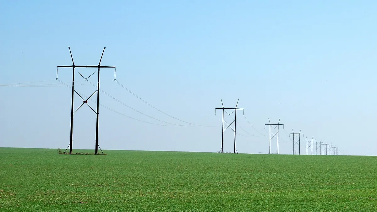 Electric power lines crossing a green field.