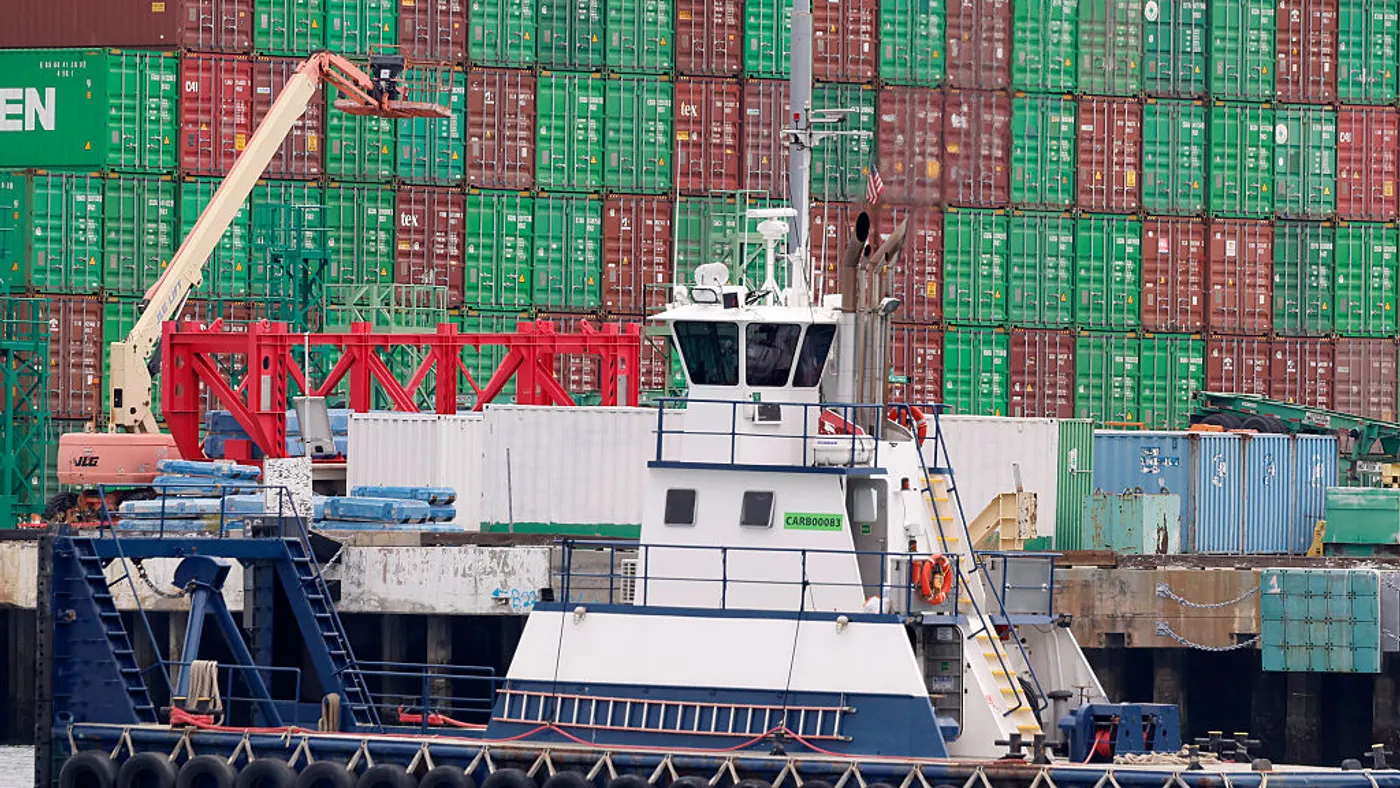 A tugboat passes shipping containers.