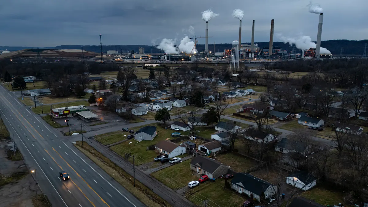 A power plant emitting smoke from smokestacks surrounded by a neighborhood with a street in the foreground.