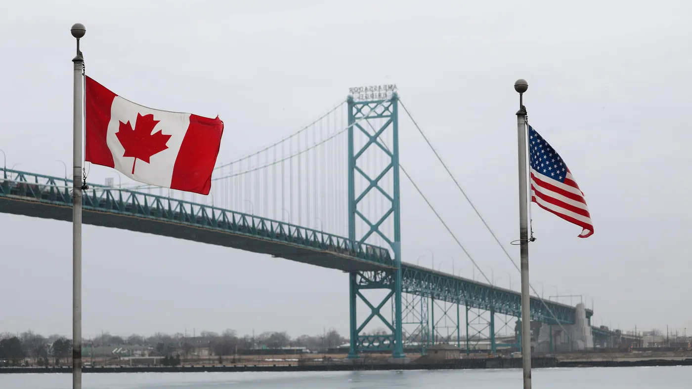 The US and Canada flags wave in front of a bridge