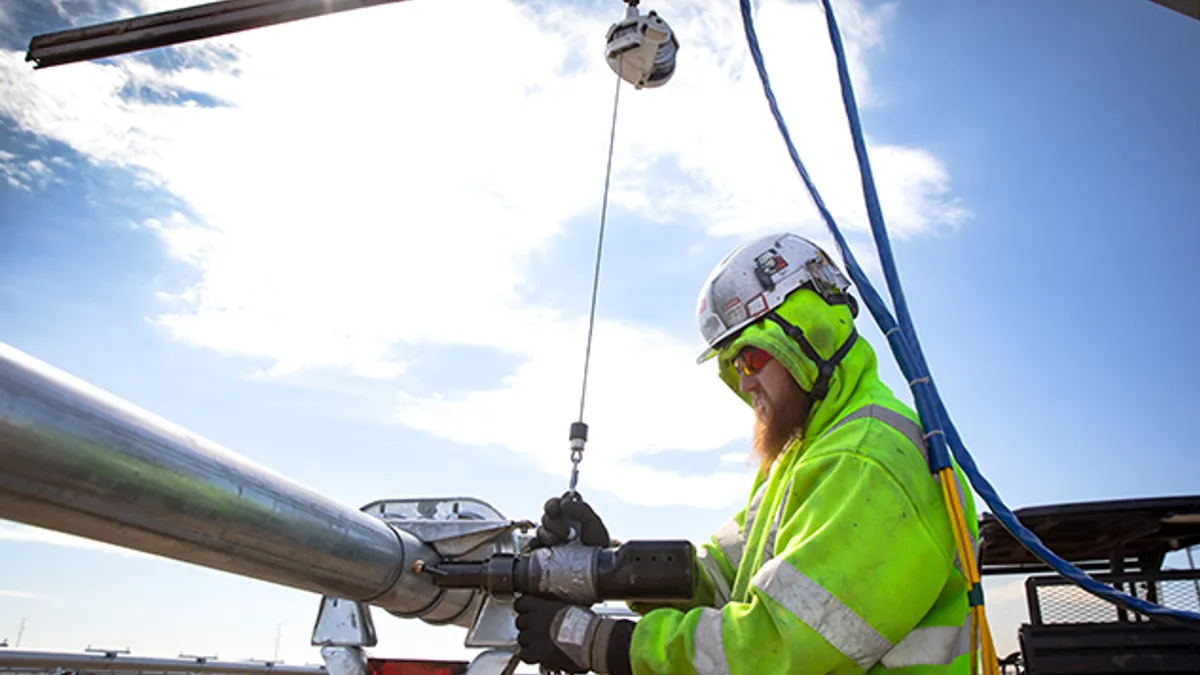 A man puts a claw-shaped tool around a pipe while working in a solar field.