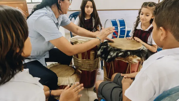 Woman teacher instructing child students to play drum in school classroom