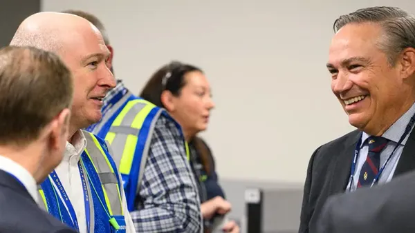 A person in a blue and yellow vest speaking to another person in a three piece suit.