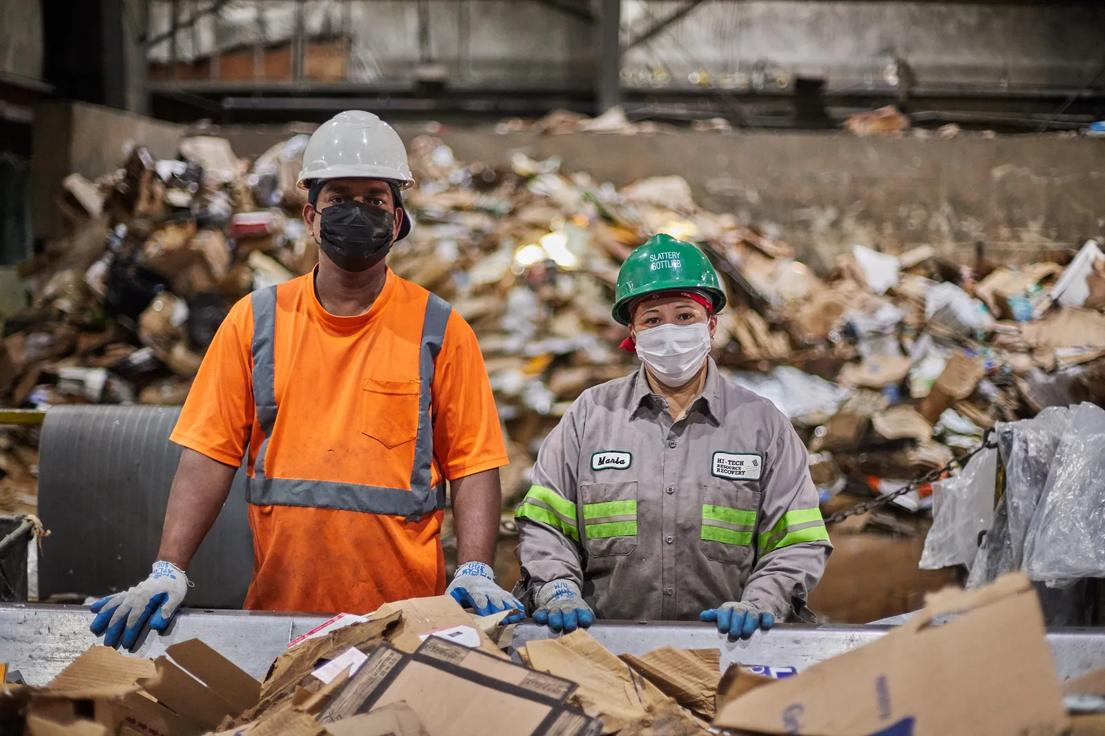 Two workers in hard hats stand over a recycling sorting line at an industrial facility in Brooklyn