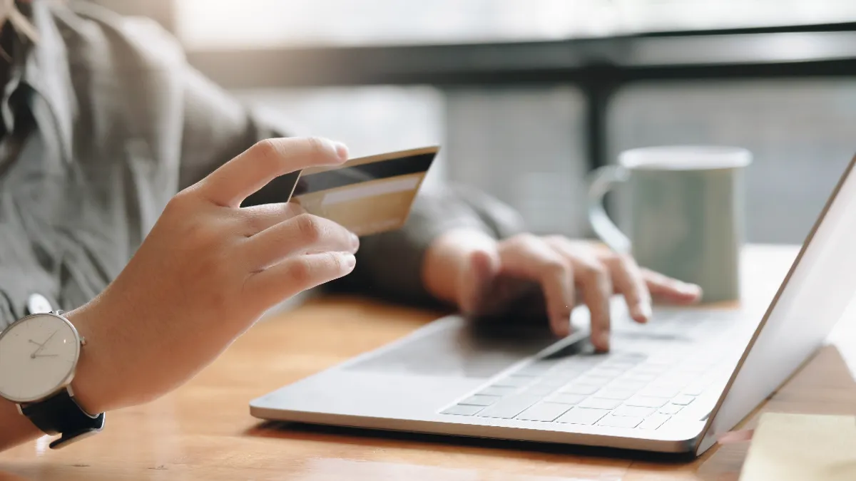 A picture of a woman holding up a credit card in front of a laptop.