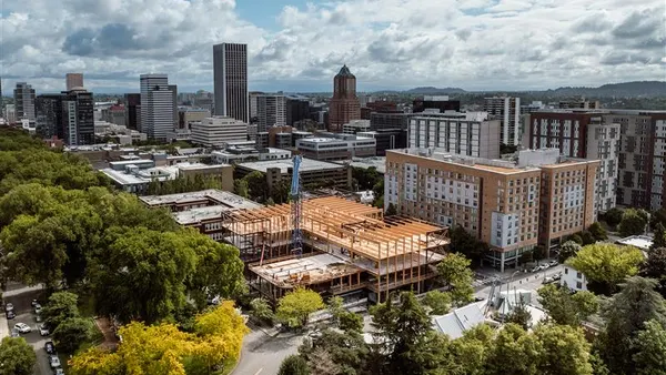 An aerial shot of an under-construction, wooden building amid a nest of other, fully constructed buildings.