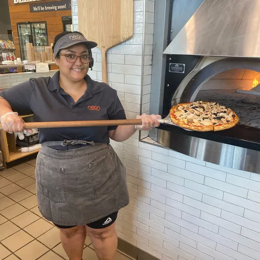 A photo of a person using a wooden paddle to take a pizza out of an oven.