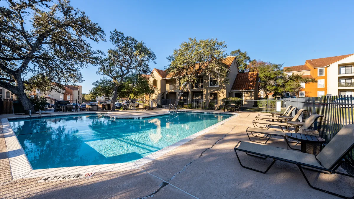 Pool and chairs in the foreground and an apartment community in the background.