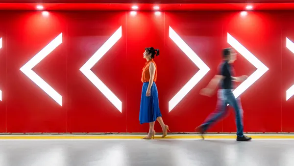 A man and woman walking towards the opposite directions of arrows in front of a red wall.