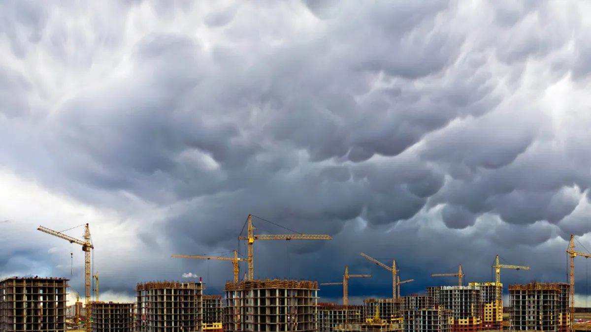 Several skyscraper buildings with cranes attached to the top of the building, with an approaching storm in the sky