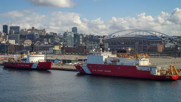Two large ships are nearby a dock with a city in the background.
