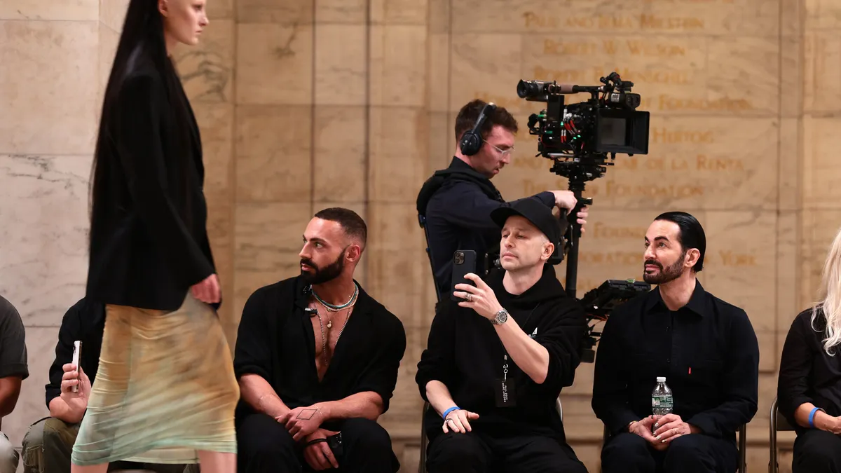 A model wearing Marc Jacobs walks while several people sit and watch in a row.