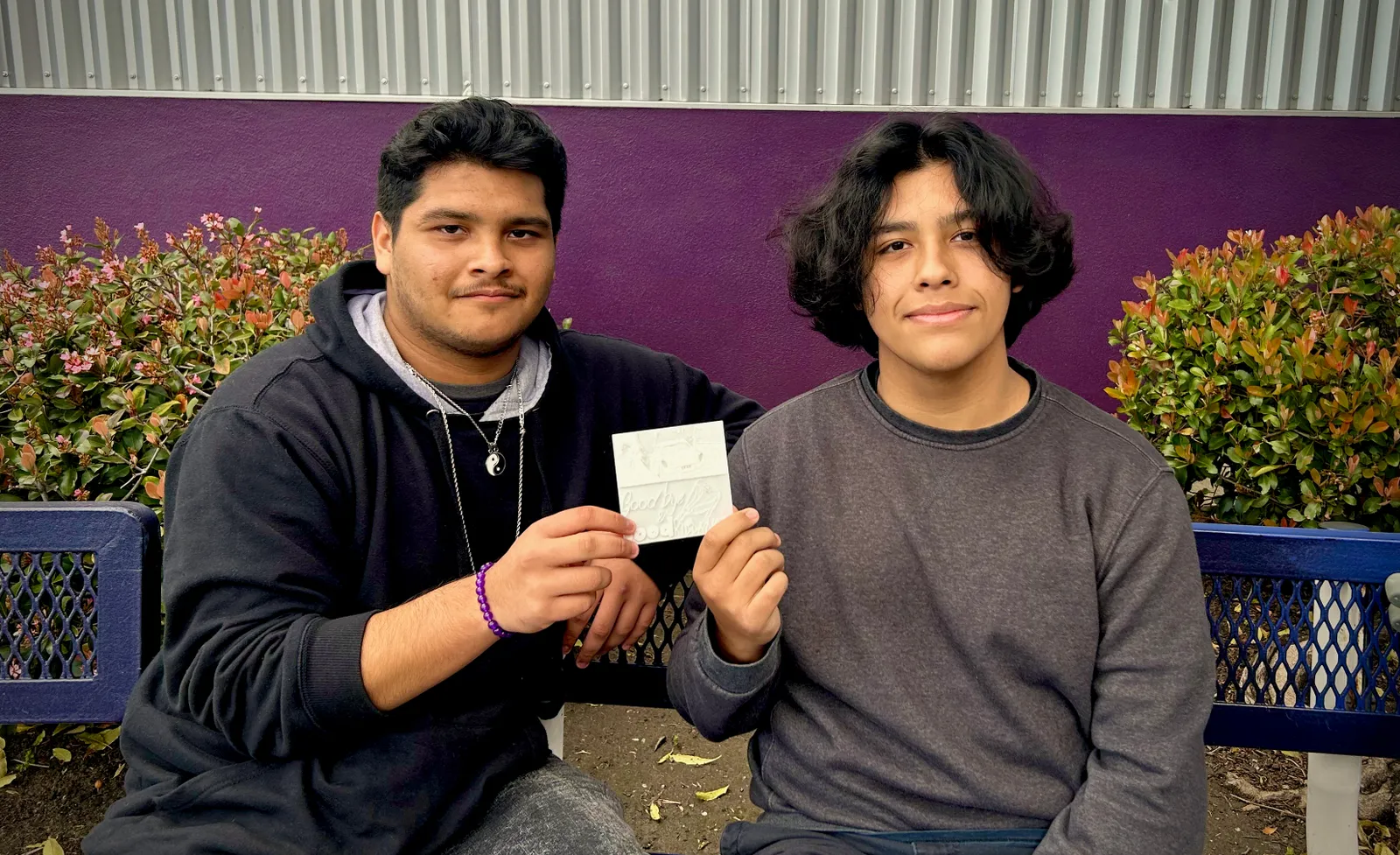 Two high school students hold a piece of paper while looking at the camers