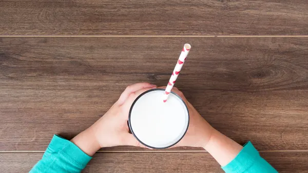 An aerial view of a child's hands holding a glass of milk on a wooden table.