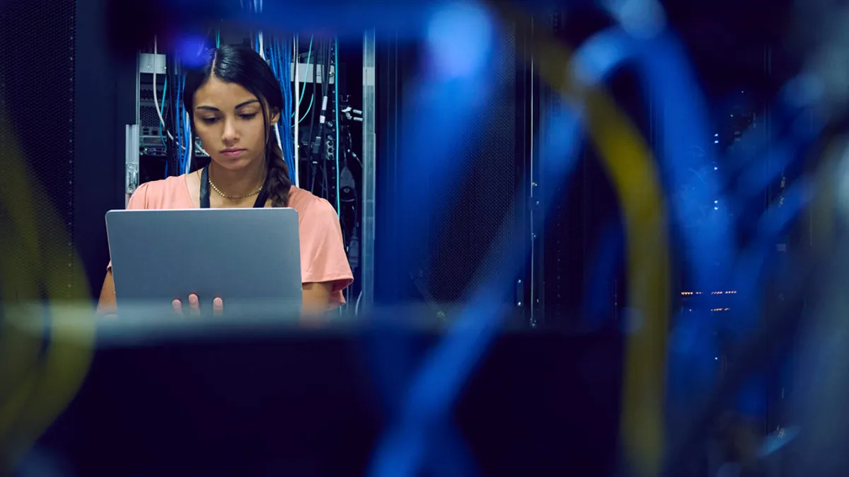 Female technician using laptop in server room.