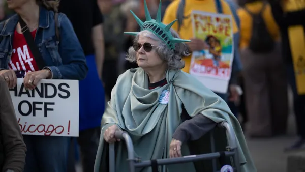 A person wearing a Statue of Liberty costume leans on their walker next to a person holding a sign that says "Hands Off Chicago."