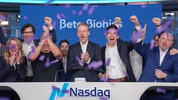 People clap and cheer behind a podium with the words "Nasdaq."