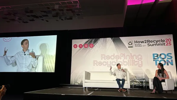 Two people sit on stage in front of a background that reads "Redefining Recyclability"