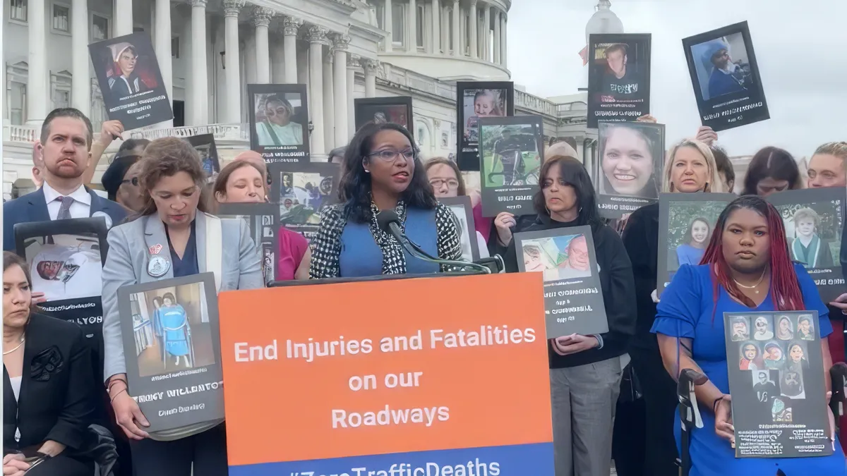 A woman speaker at a podium with many people behind her carrying posters standing in front of the U.S. Capitol.