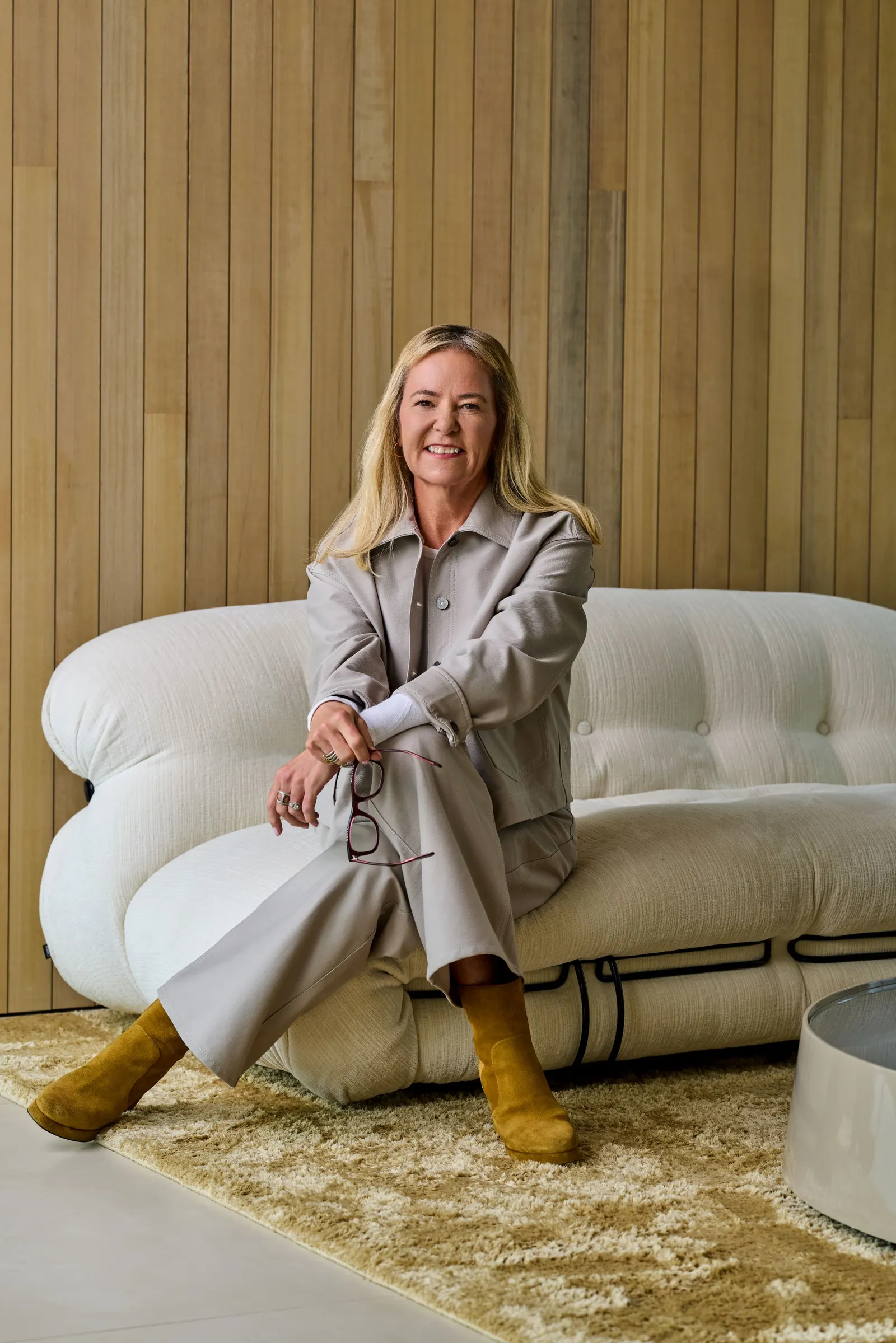 Heidi O'Neill sits on a bench in front of a pale wood wall.