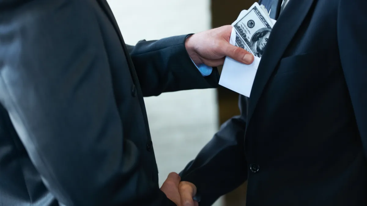 Two corporate businessmen shaking hands while one man places money in the other's pocket.