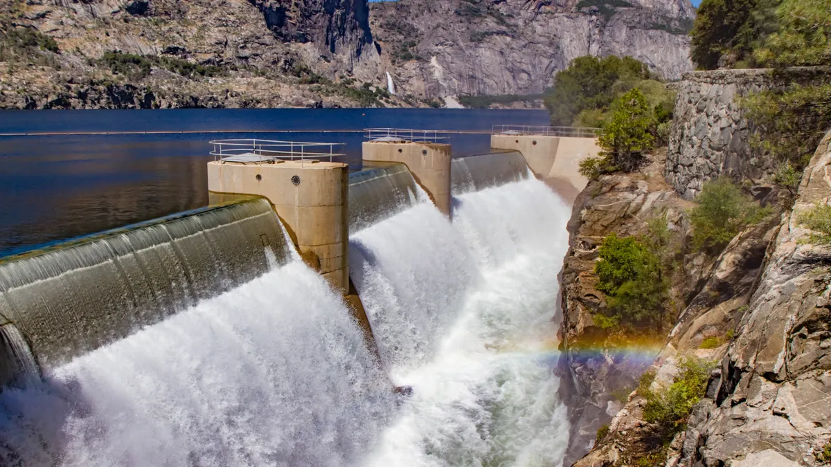 O'Shaughnessy (Hetch Hetchy) Dam in Yosemite National Park, California, USA. Water gushing forth from the dam with slight rainbow in foreground, cobalt blue water in mid grou