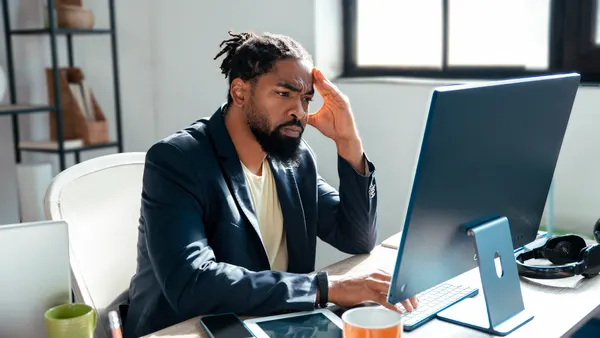 A man sits in front of a computer with a hand on his head.