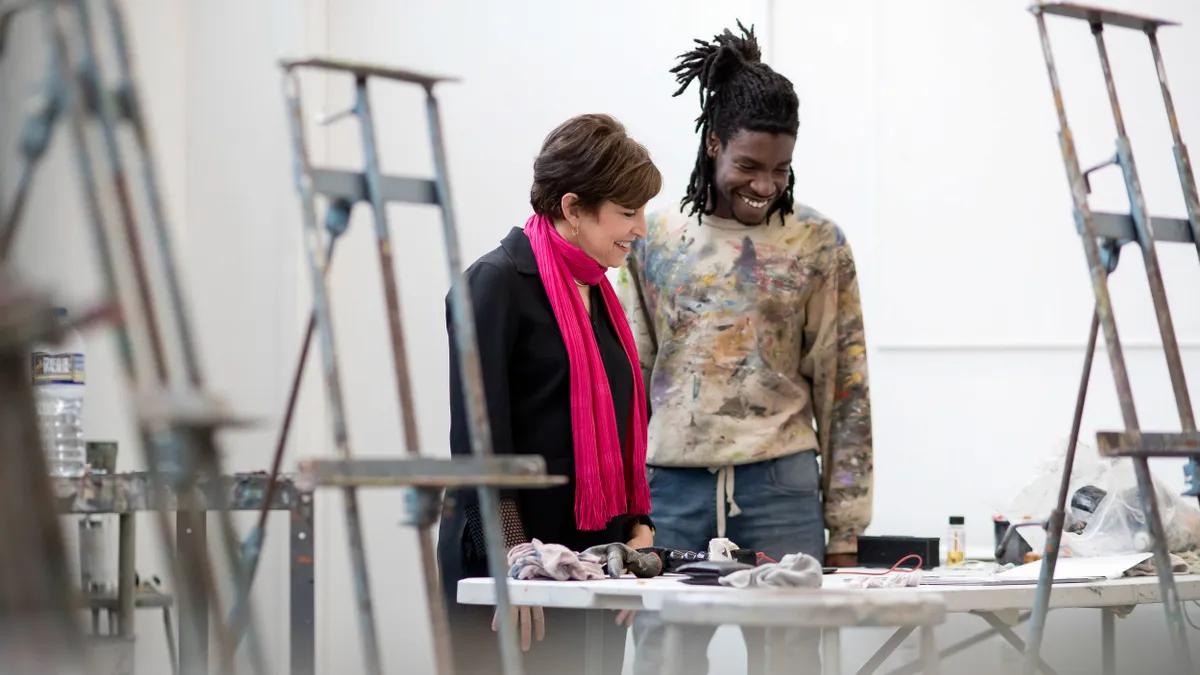 Woman on left and man on right discuss project on a work table in art studio.