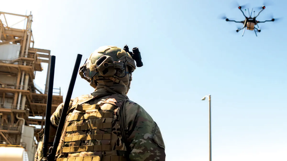 A soldier looks up at a drone in the sky.