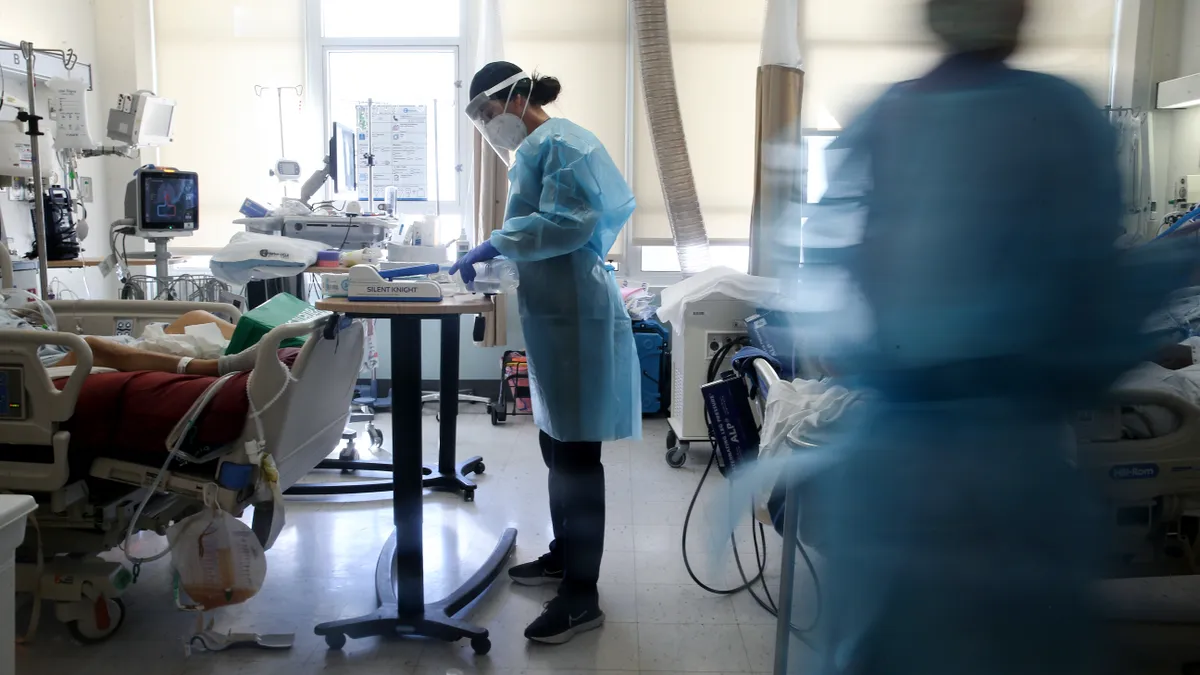 A surgeon stands in a hospital room bending over a small table of medical instruments