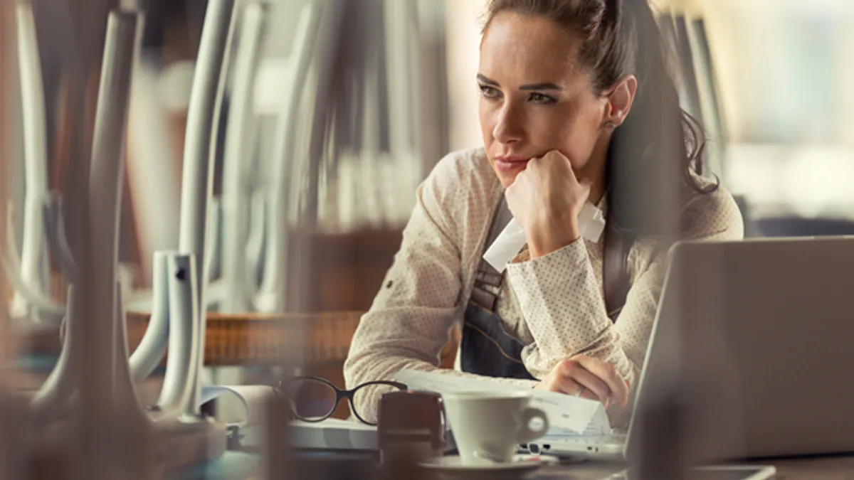 Unhappy female pub owner sits over computer and coffee