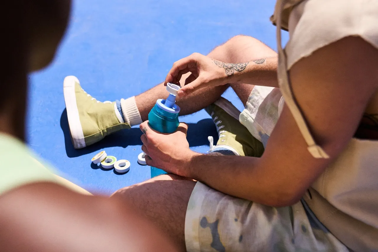 A person sitting on the ground puts a scent pod on an Air Up water bottle.