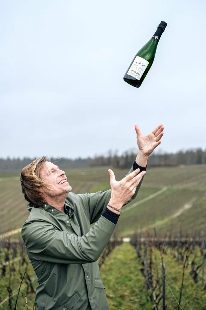 Man throwing bottle of champagne up in the air while standing in a a field