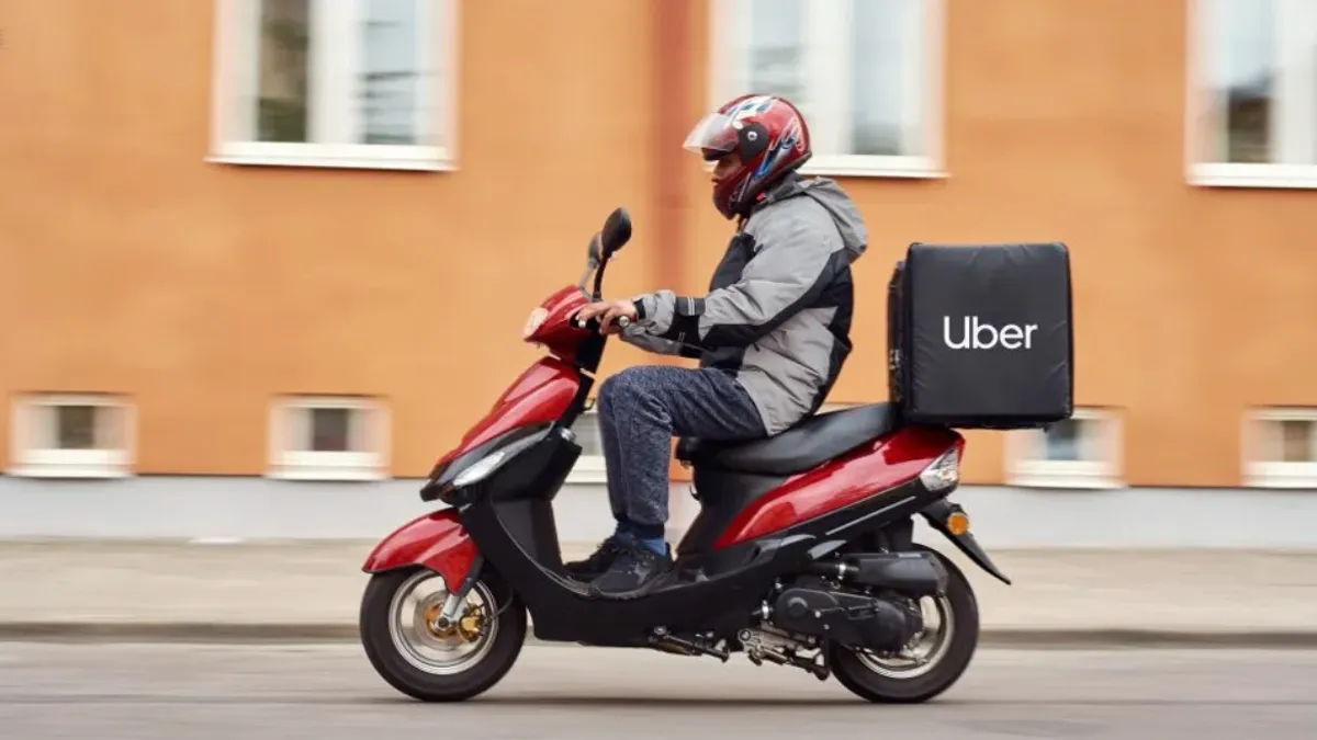 An Uber driver on a red moped delivers items to a customer.