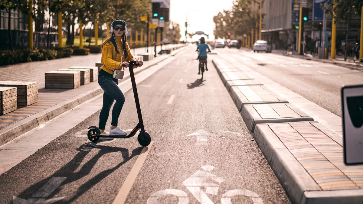 A woman ride an e-scooter in a protected bike lane.