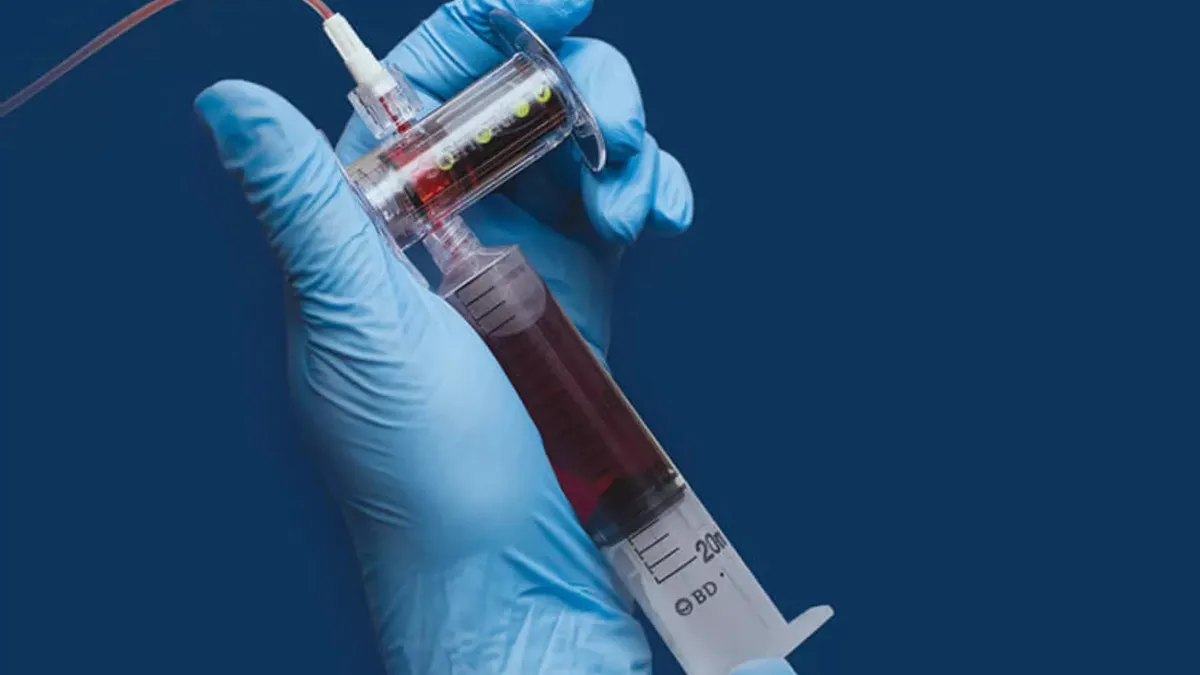 A healthcare worker holds a syringe for collecting blood in a gloved hand.