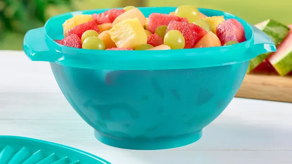 Tupperware bowl full of fruit on a table.