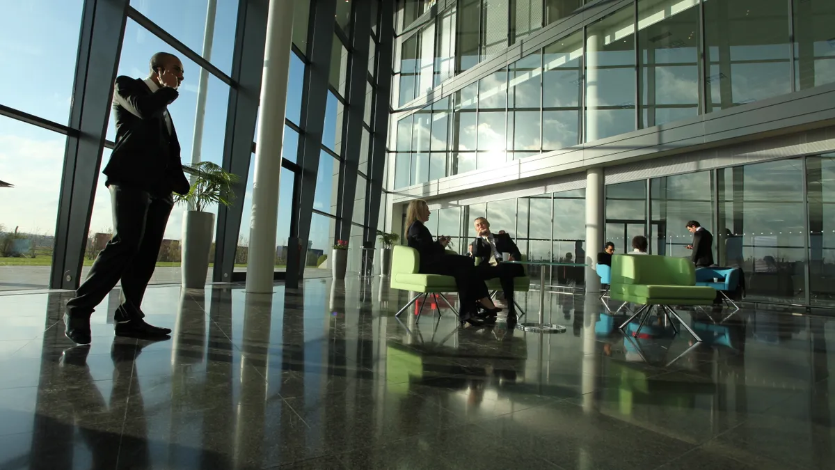 Large office atrium with bright morning sunlight shining on business people as they start their day. A corporate scene captured on Canon 5D MK2 with 14mm lens.