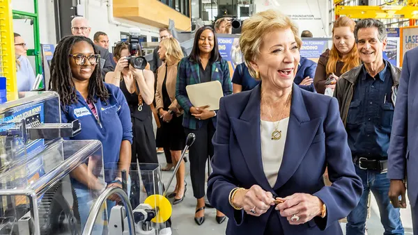 A person is walking through a manufacturing floor, other people are gathering around and behind them.