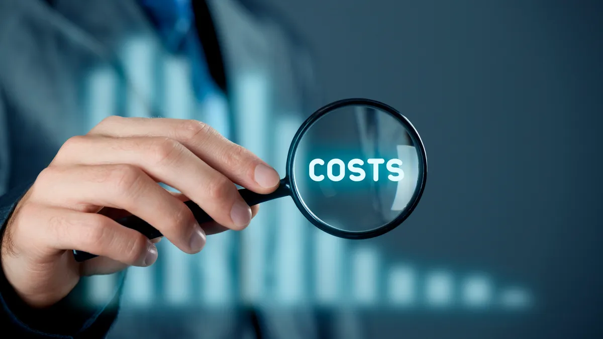 Focus on decrease (cut) costs concept. Businessman with magnifying glass enlarge word costs. Graph with decreasing costs on background.