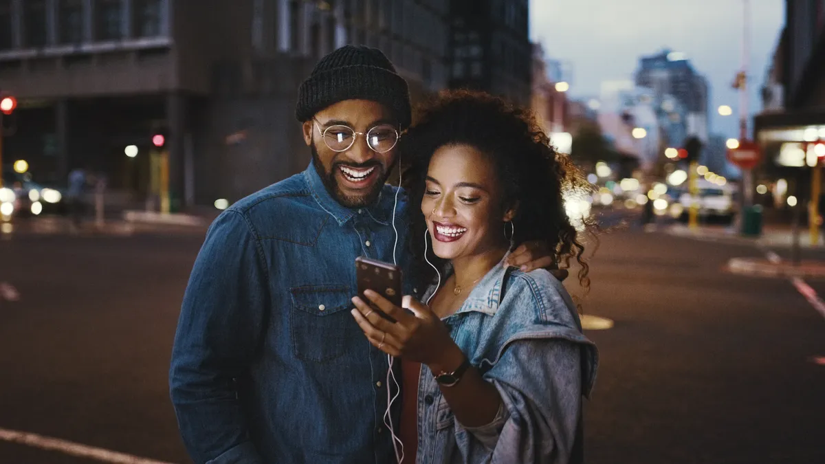 Shot of a young couple using a smartphone and earphones in the city