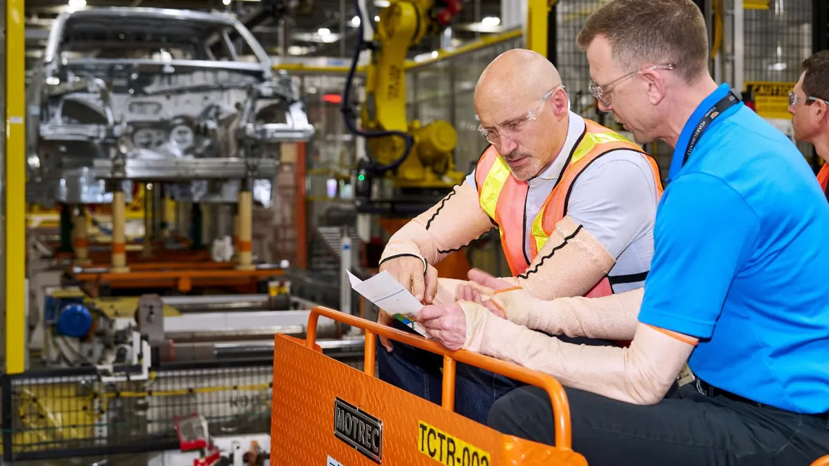 Sterling Anderson wearing protective arm wear, looking over a document with another person inside GM's Factory Zero in Michigan.