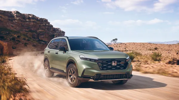 A light green 2026 Honda CR-V TrailSport Hybrid SUV driving on a dusty desert road.