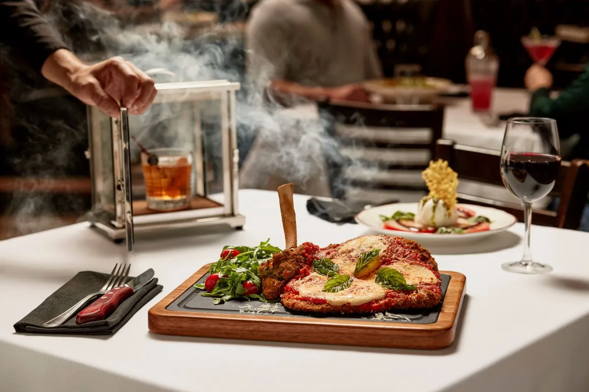 An image of a veal parmesan chop with marinara sauce and mozzarella on a dark table.