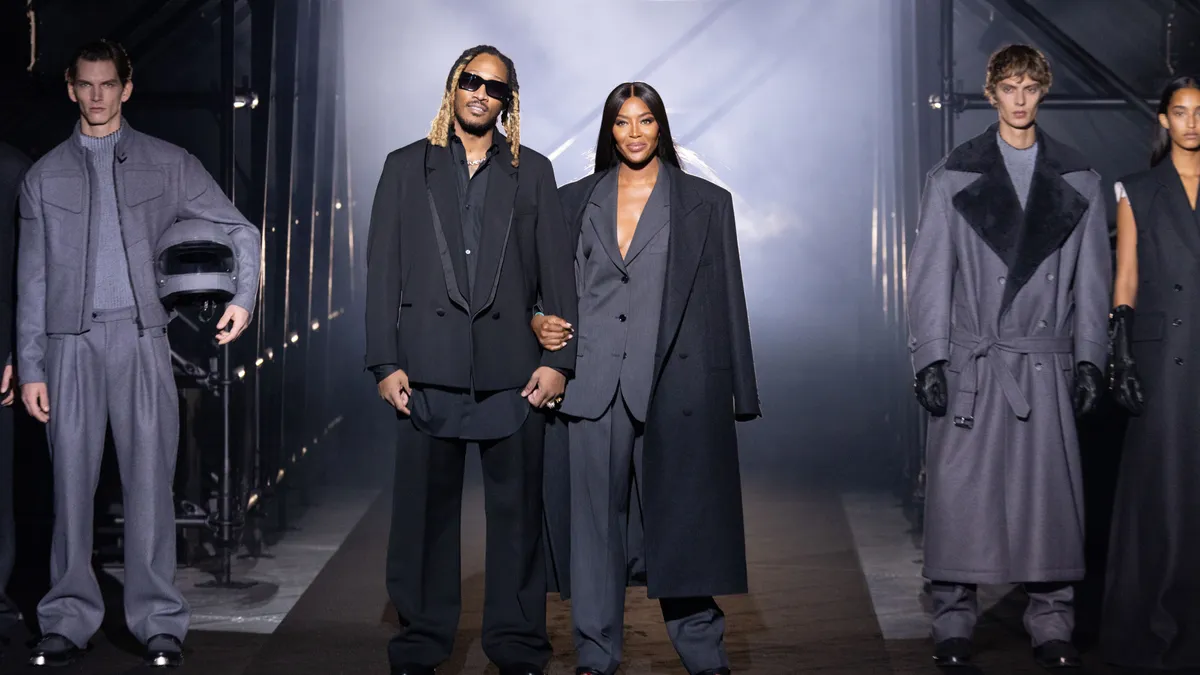 Two people hold hands and face the camera wearing gray suits, flanked by models also wearing gray suiting separates.