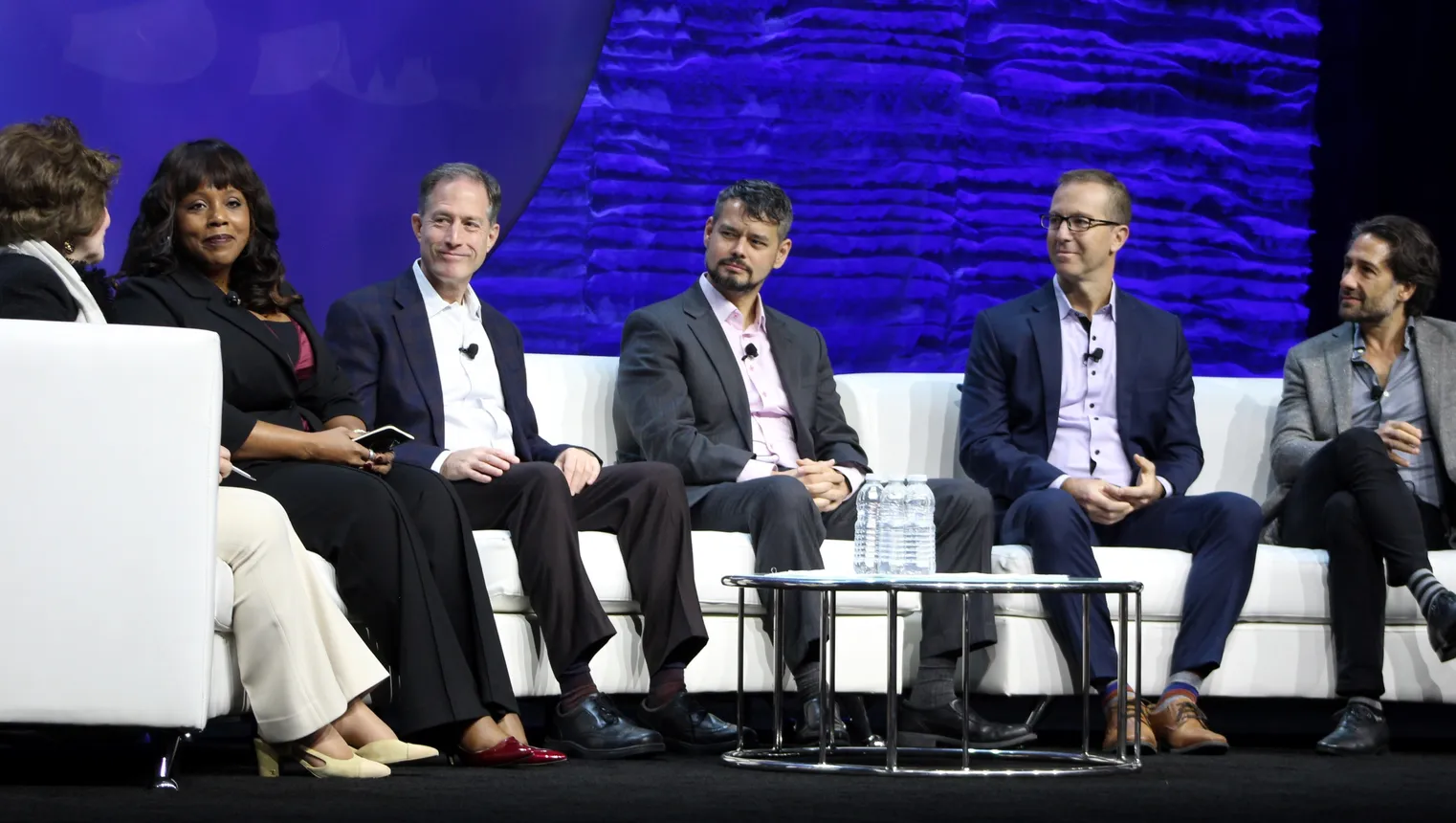 Six people sit on a curved couch around a table.