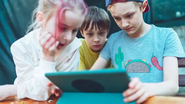 Three children playing games at digital tablet.