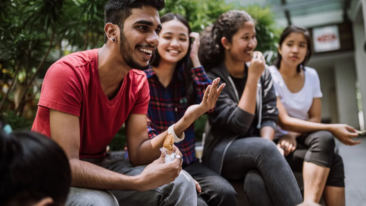 A group of four young adults sit on a bench and talk among themselves.